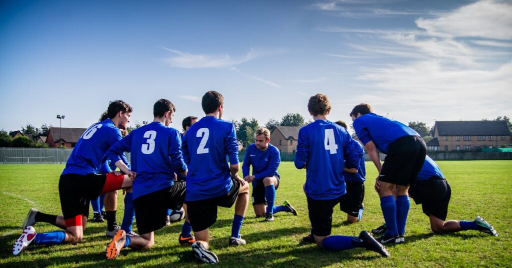 A group of male football players in blue uniforms huddle on a grassy field before a match.